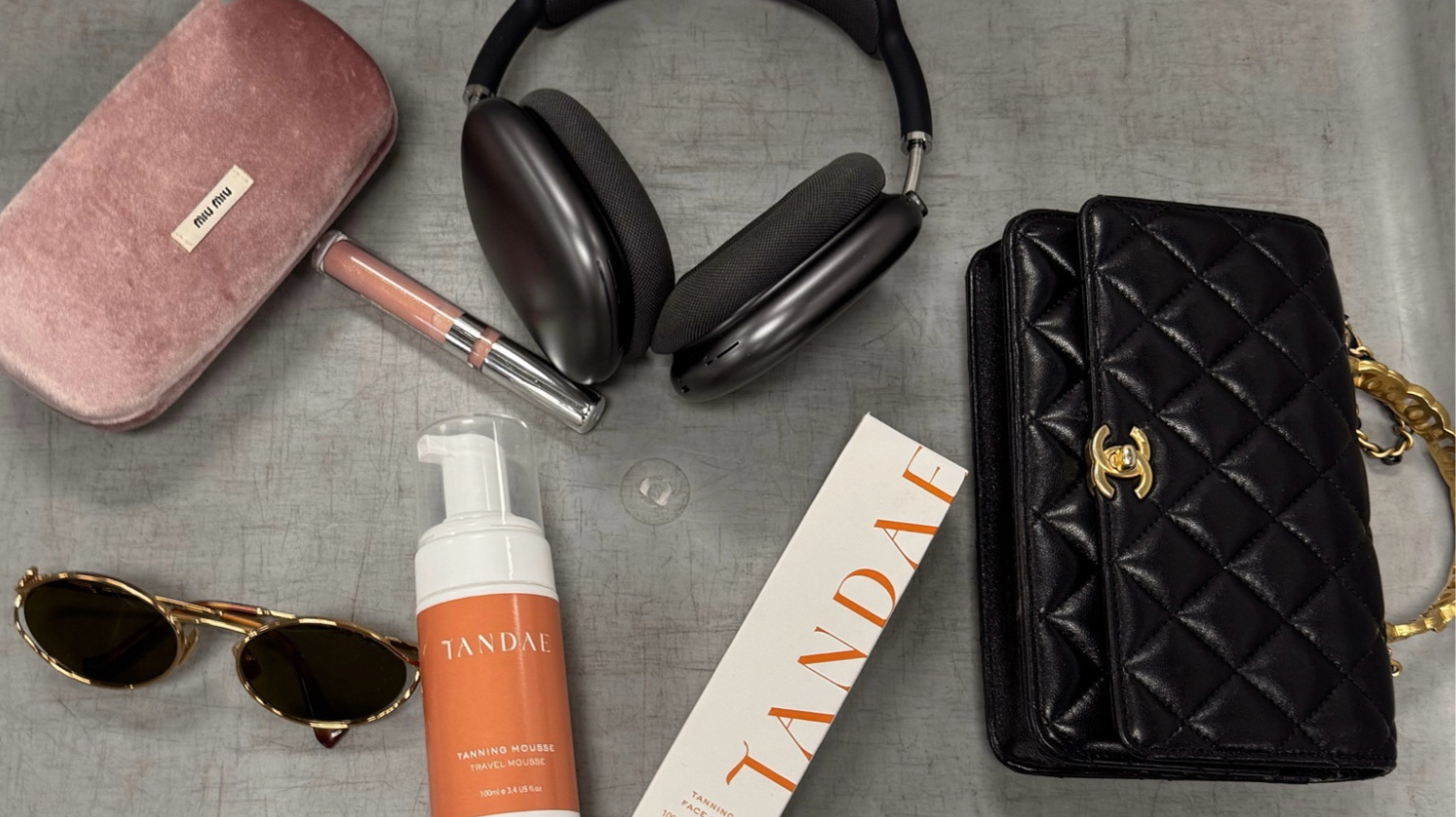 Airport security tray with sun glasses, Chanel handbag, headphones and Tandae Tanning Mousse Travel Bottle