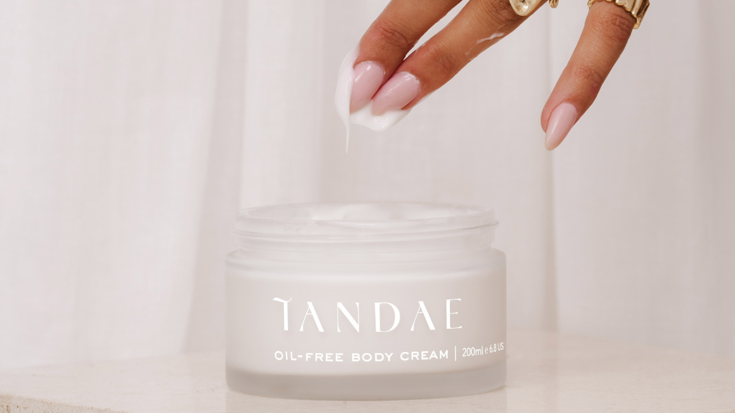 Image of the Tandae Oil-Free Body Cream and a hand that's just dipped into the formula